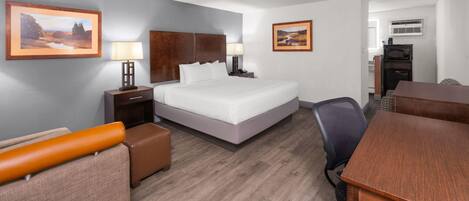 A hotel room with a bed, a desk, a chair, a lamp, a nightstand, and two framed pictures on the wall.