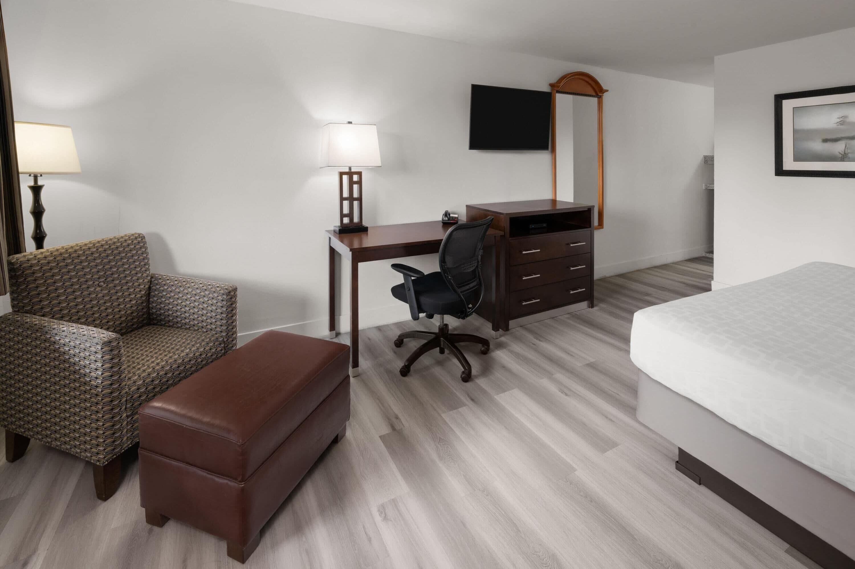 A hotel room with a bed, a desk with a chair, a sofa, a dresser, a lamp, and a TV.
