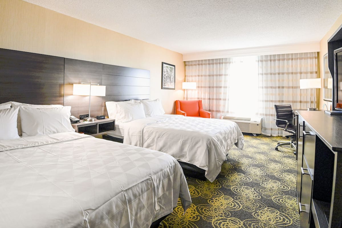 A hotel room with two beds, a desk, a chair, a TV, and a window with curtains.
