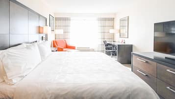 Habitación de hotel con una cama grande, un escritorio con silla, un televisor y una ventana con cortinas.