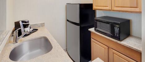 A compact kitchen with a stainless steel refrigerator, a built-in microwave, and a coffee maker.