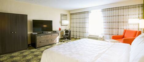 A hotel room with a large bed, a desk with a flat-screen TV, a chair, and a wardrobe.