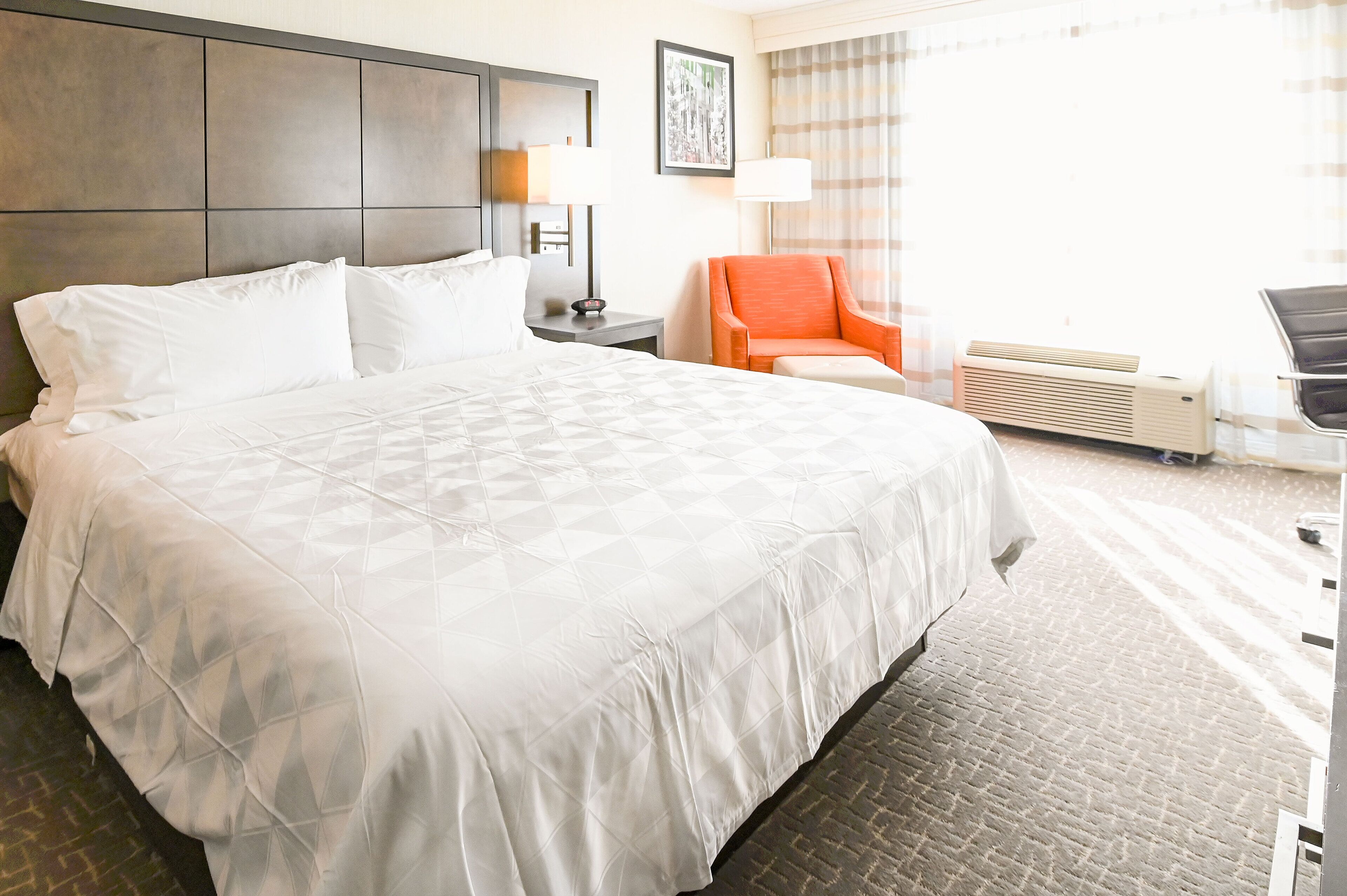 A hotel room with a large bed, a chair, a desk, and a window with curtains.