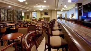 A hotel lobby with multiple seating areas, a bar, and a television screen. - Holiday Inn Charlottesville-Univ Area by IHG (Charlottesville)
