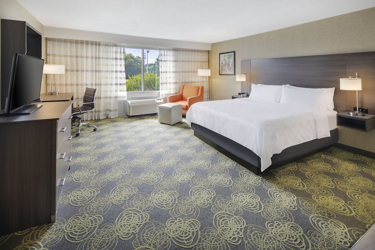 A hotel room with a large bed, a desk with a TV, a chair, and a window with curtains.
