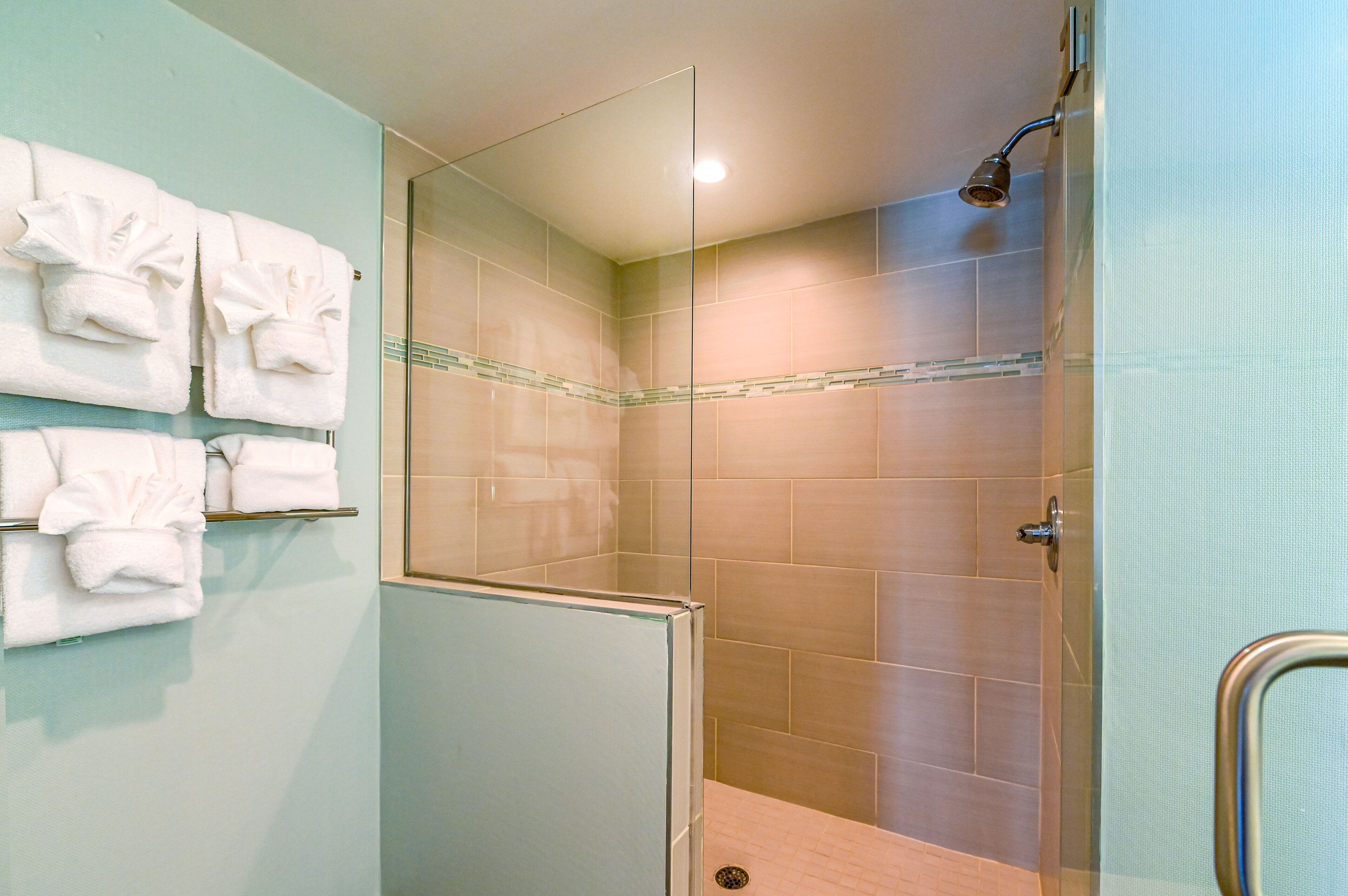 A glass-enclosed shower with beige tiles, a glass door, and a towel rack with folded towels.