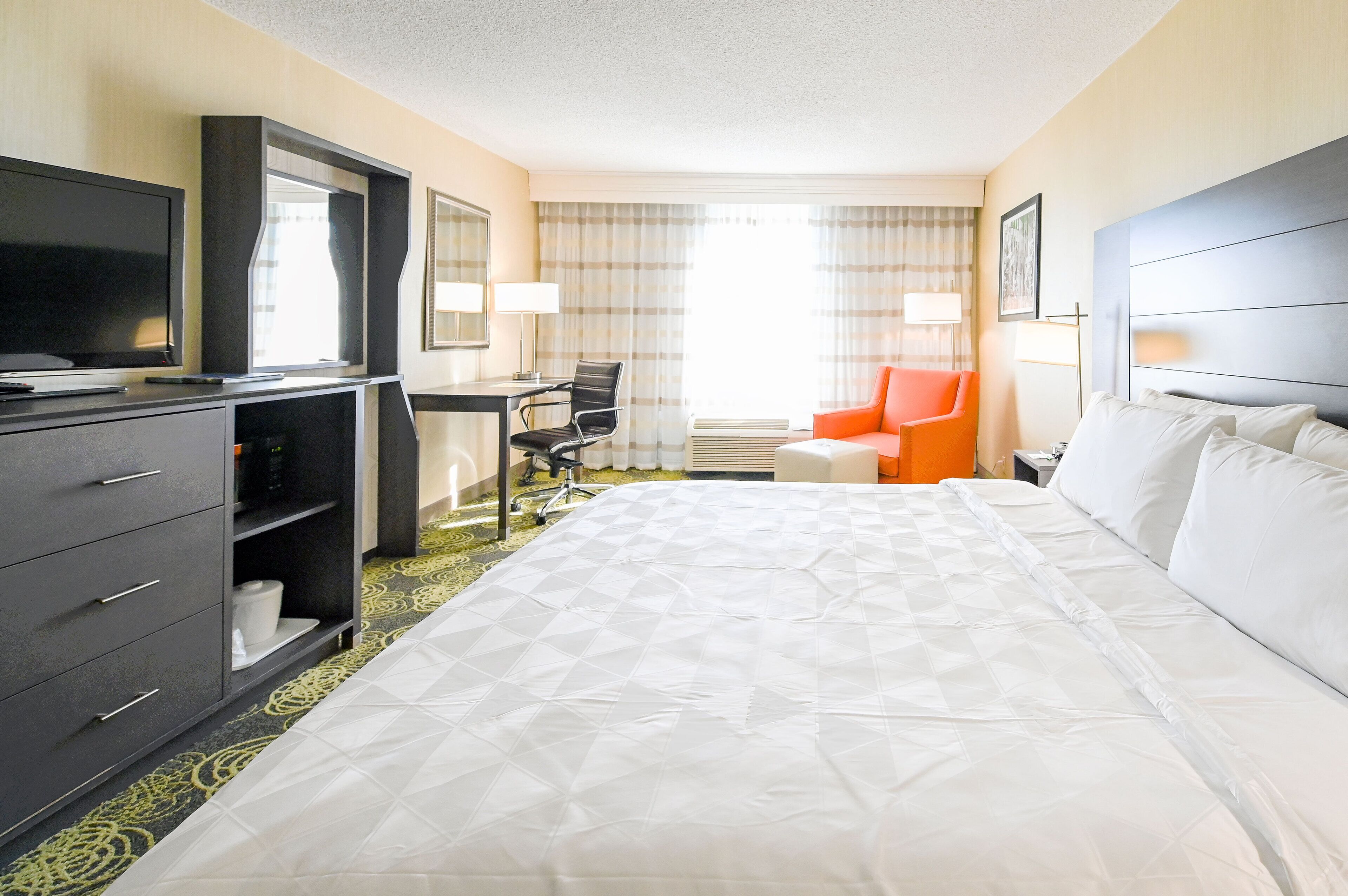 A hotel room with a large bed, a desk with a chair, a television, and a wardrobe.