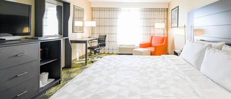 A hotel room with a large bed, a desk with a chair, a television, and a wardrobe.
