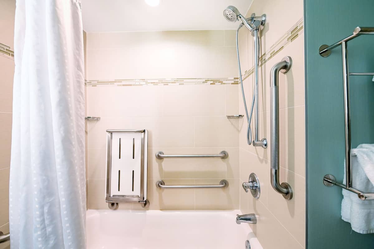 A bathroom with a bathtub, grab bars, a showerhead, and a towel rack.