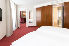 Una habitación de hotel con una cama grande, un armario, un escritorio con una silla y un baño visible a través de una puerta abierta.