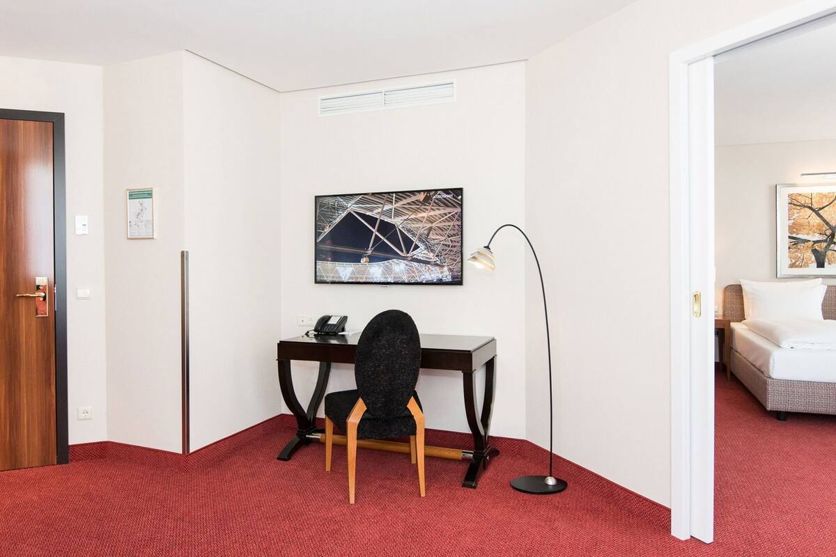 A hotel room with a desk, chair, and artwork on the wall.