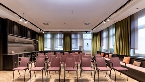 Un salón de conferencias con filas de sillas, una pantalla de proyección y un ventanal con cortinas.