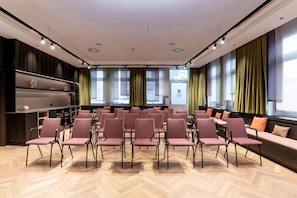 Un salón de conferencias con filas de sillas, una pantalla de proyección y un ventanal con cortinas.