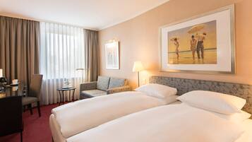 Ein Hotelzimmer mit zwei Betten, einem Schreibtisch, einem Stuhl, einem Tisch und einem Gemälde an der Wand.