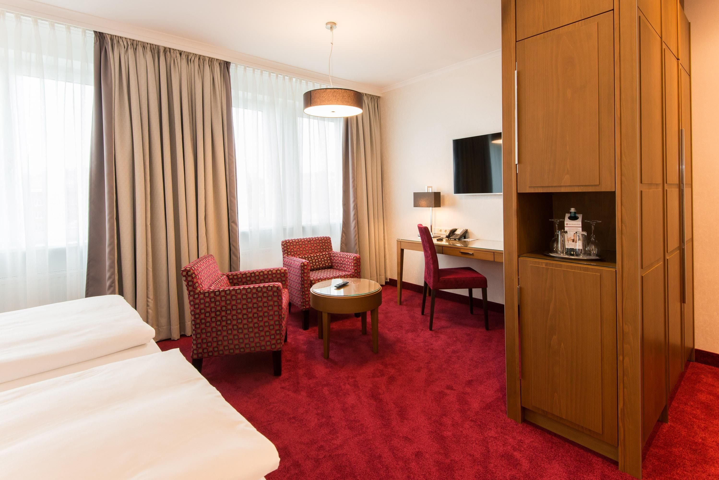 Habitación de hotel con cama, dos sillones, escritorio, televisor y minibar.