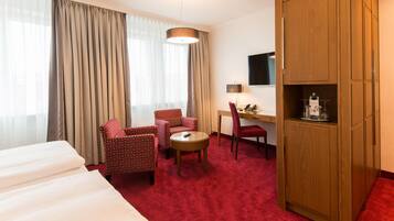 Habitación de hotel con cama, dos sillones, escritorio, televisor y minibar.
