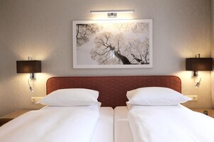 Ein Hotelzimmer mit Doppelbett, zwei Nachttischlampen, einem gerahmten Bild an der Wand und einem modernen Kopfteil.