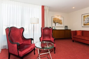 A hotel room with a red sofa, two red armchairs, a glass coffee table, a desk with a lamp, and a painting on the wall. - Best Western Plus Hotel St. Raphael (Hamburg)