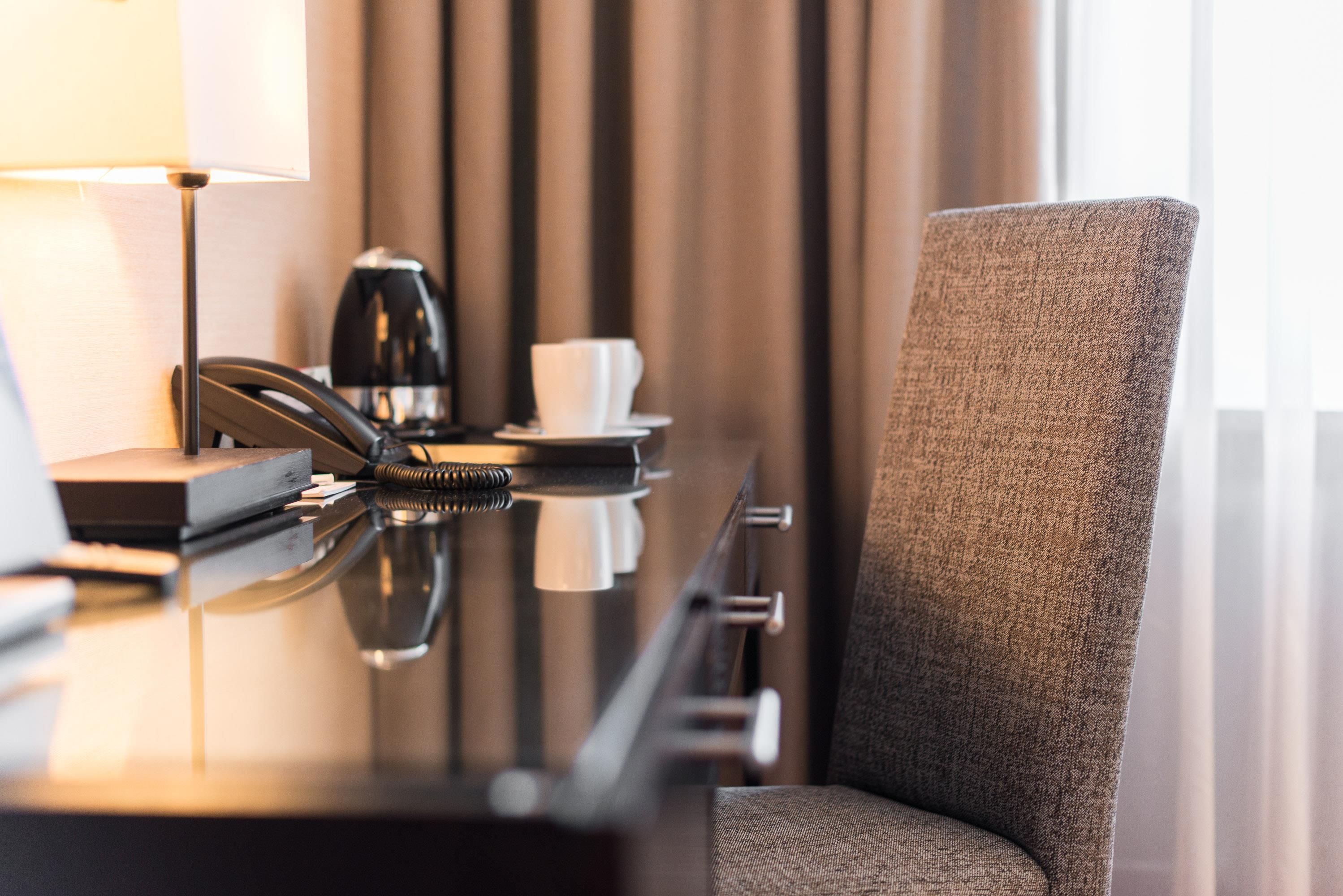 Habitación de hotel con escritorio, teléfono, cafetera y una silla.