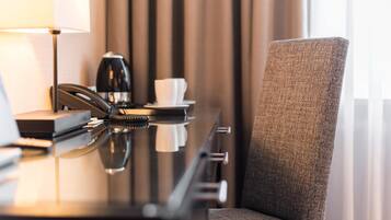 Habitación de hotel con escritorio, teléfono, cafetera y una silla.