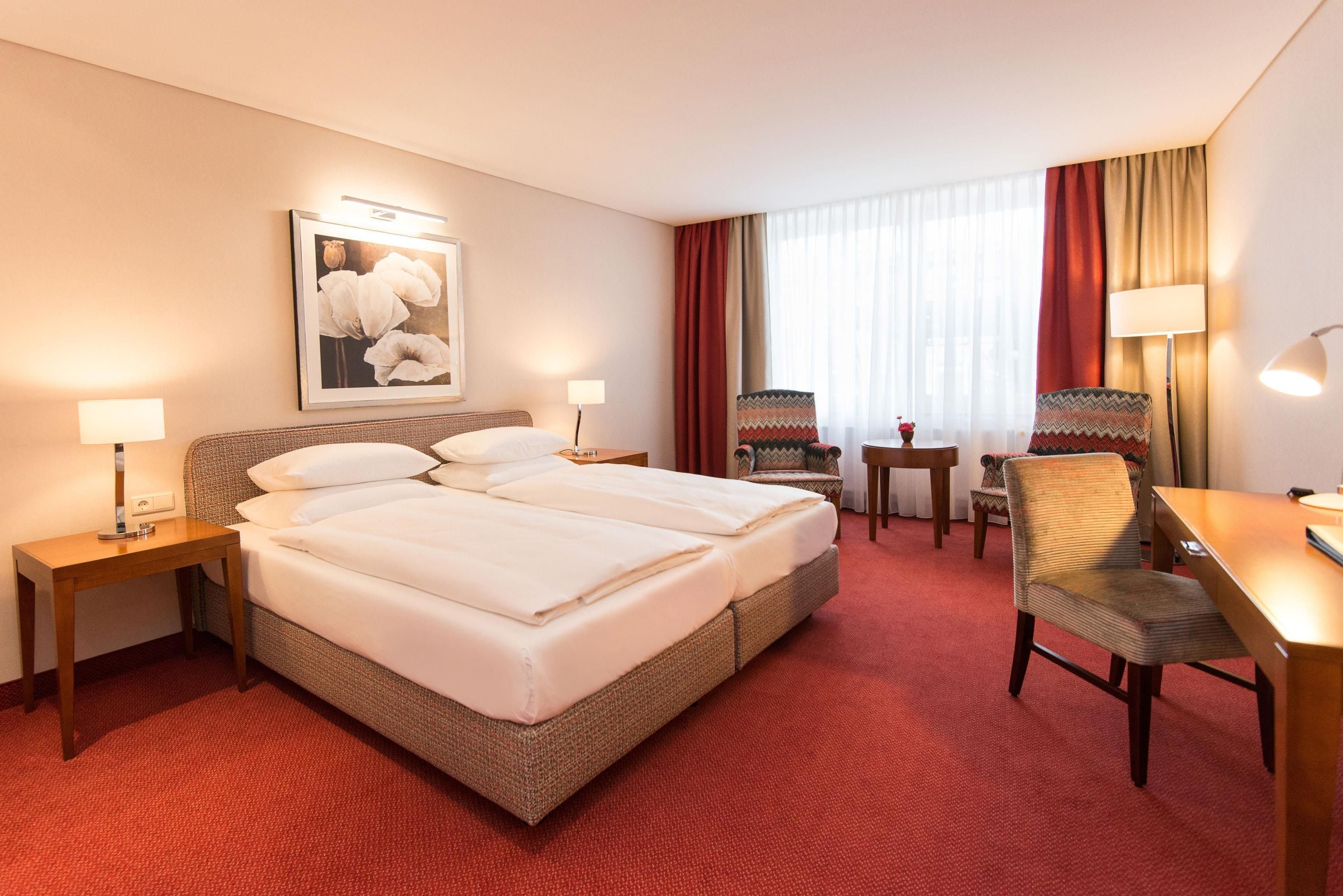 Habitación de hotel con cama doble, dos mesitas de noche, un escritorio, una silla y ventana con cortinas.