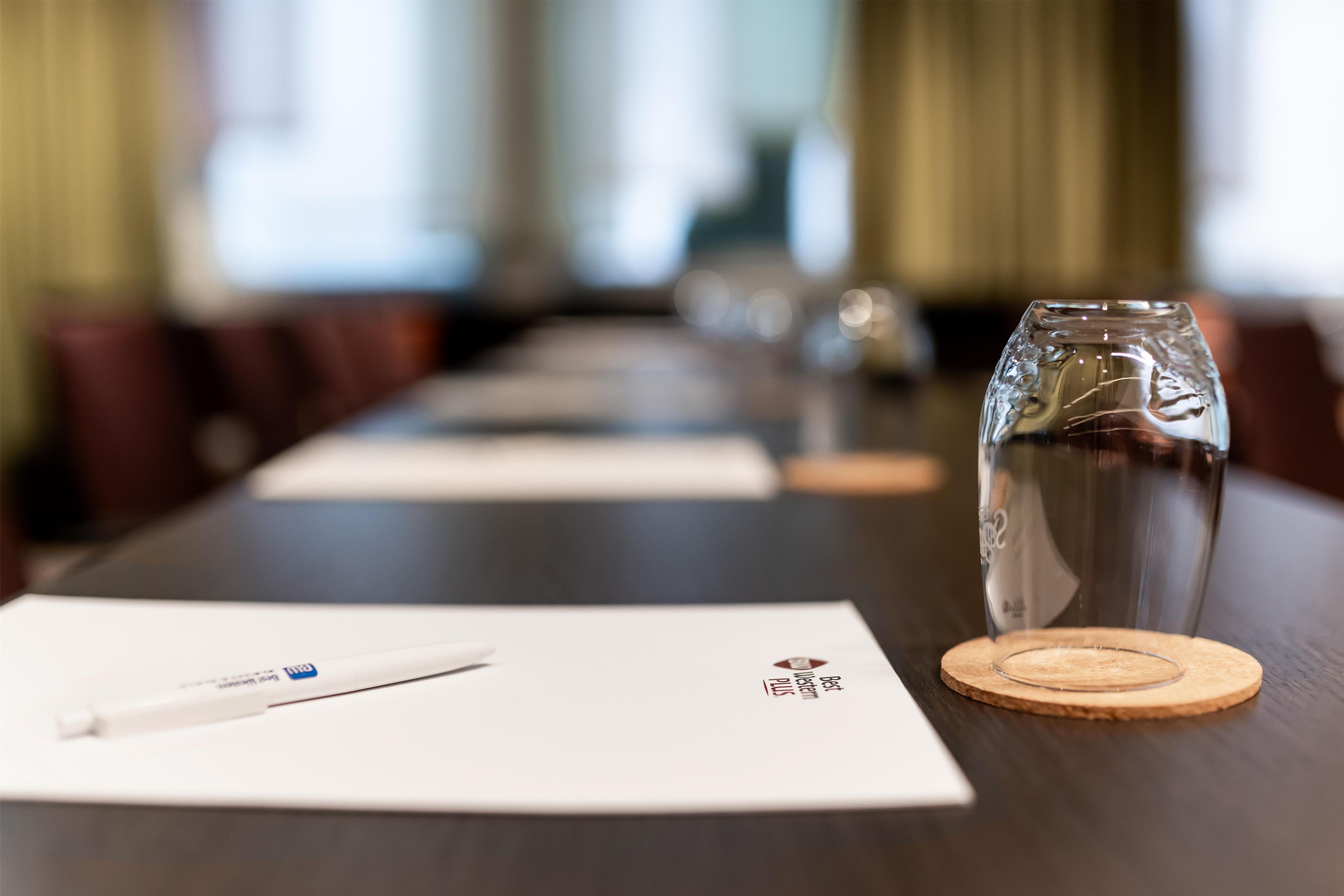 A conference table with a glass of water, a pen, and a coaster.