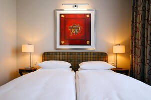Ein Hotelzimmer mit Doppelbett, zwei Nachttischlampen, einem Kopfteil mit Karomuster und einem gerahmten Kunstwerk über dem Bett.