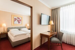 A hotel room with a bed, a desk, a chair, a TV, and a window with curtains. - Best Western Plus Hotel St. Raphael (Hamburg)