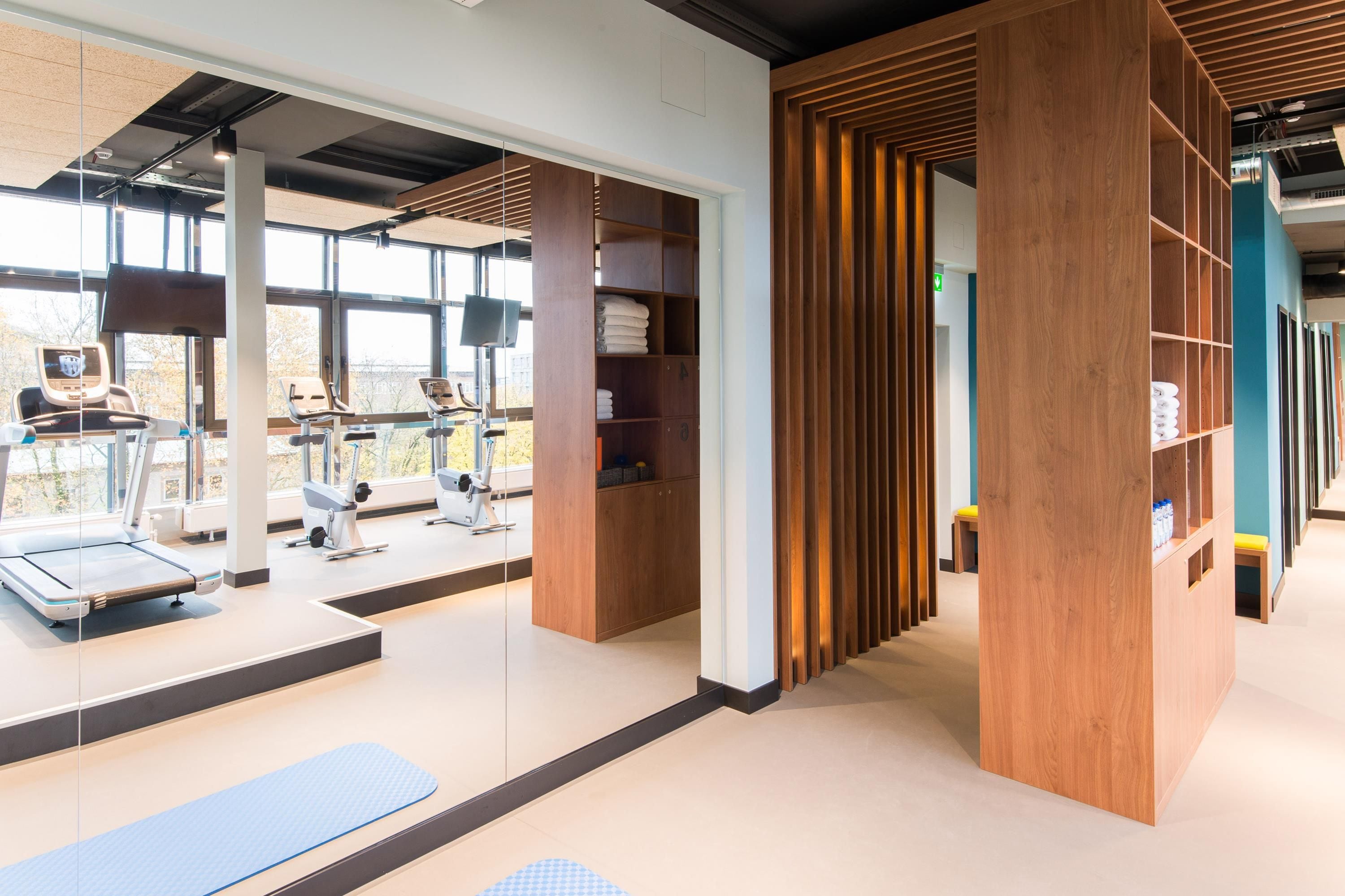 A gym with exercise equipment, wooden storage units, and a view through large windows.