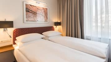 A hotel room with a double bed, two bedside tables, a wall-mounted lamp, a framed picture, and a window with curtains.