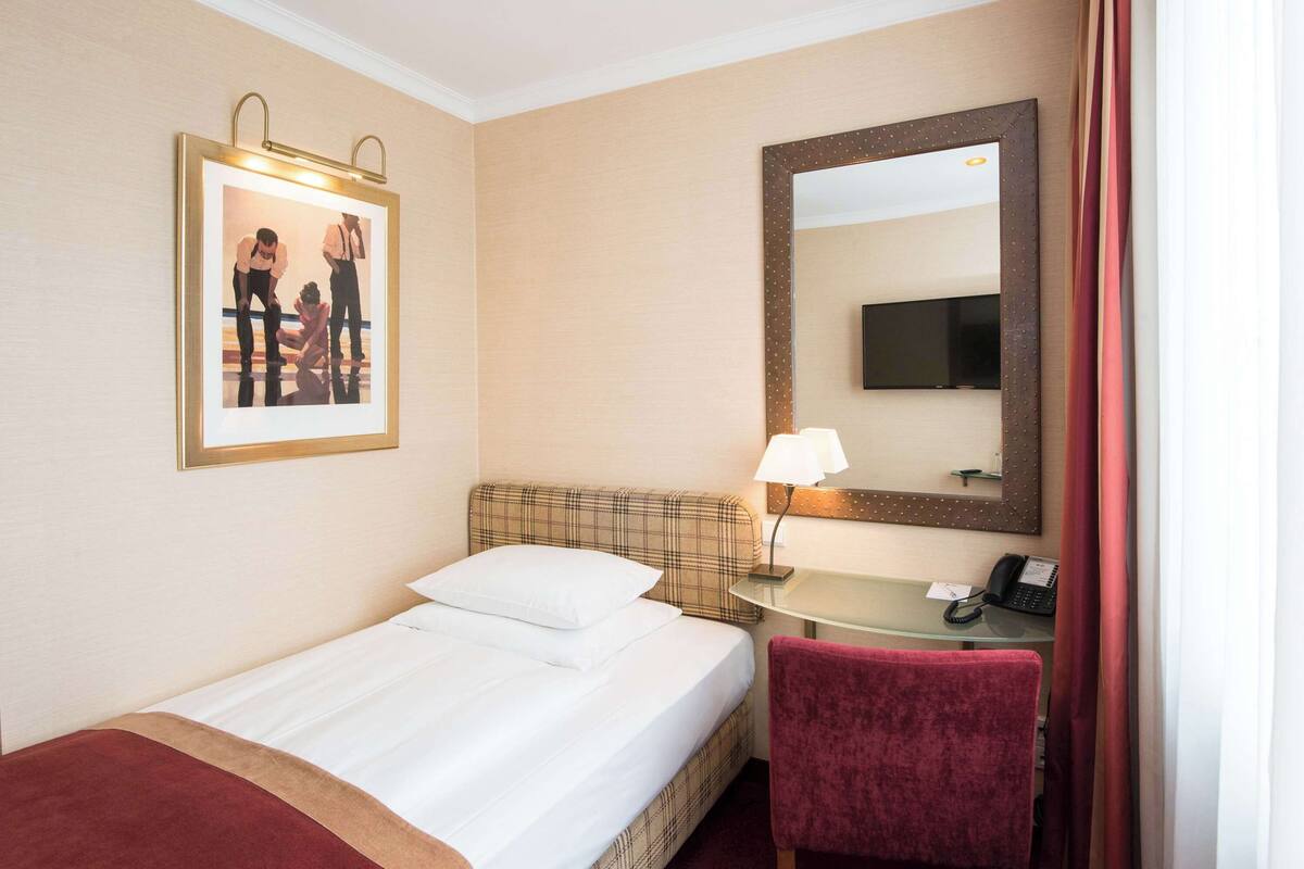 A hotel room with a bed, a desk with a telephone, a mirror, and a framed picture on the wall.