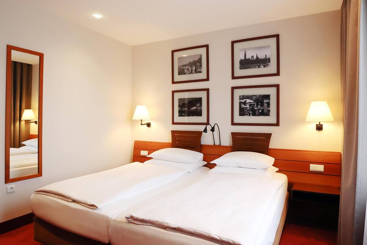 A hotel room with a large bed, two bedside tables, a mirror, and four framed pictures on the wall.