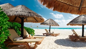 A beach with thatched umbrellas, lounge chairs, and a clear view of the ocean.