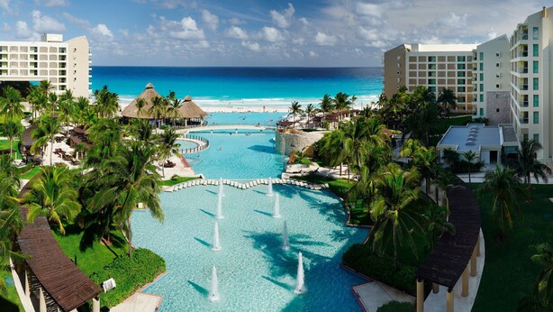 A resort with a central pool, palm trees, and a view of the ocean.