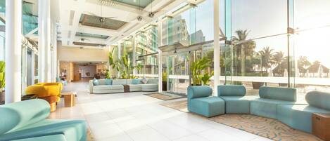A spacious lobby with modern seating, large windows, and a view of palm trees.
