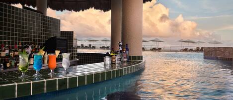 A poolside bar with various drinks and umbrellas, a tiled pool, and a view of the sky with clouds.