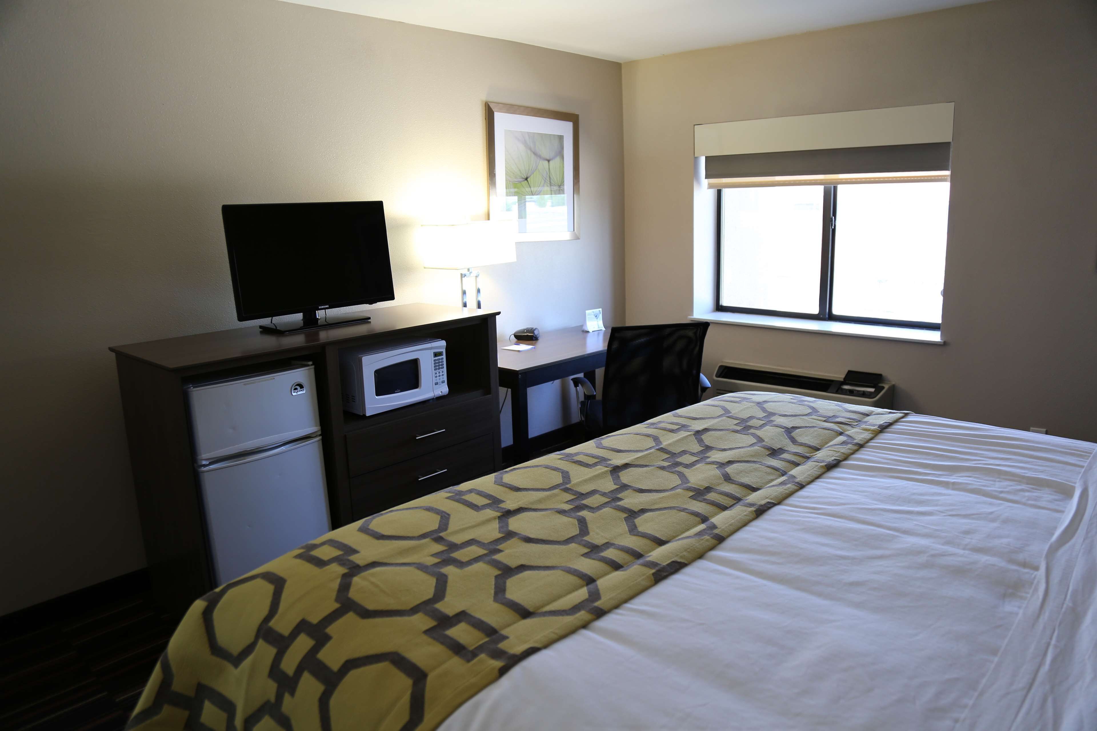 Une chambre d’hôtel équipée d’un lit, d’un bureau avec un ordinateur, d’un four à micro-ondes et d’une fenêtre avec des stores.