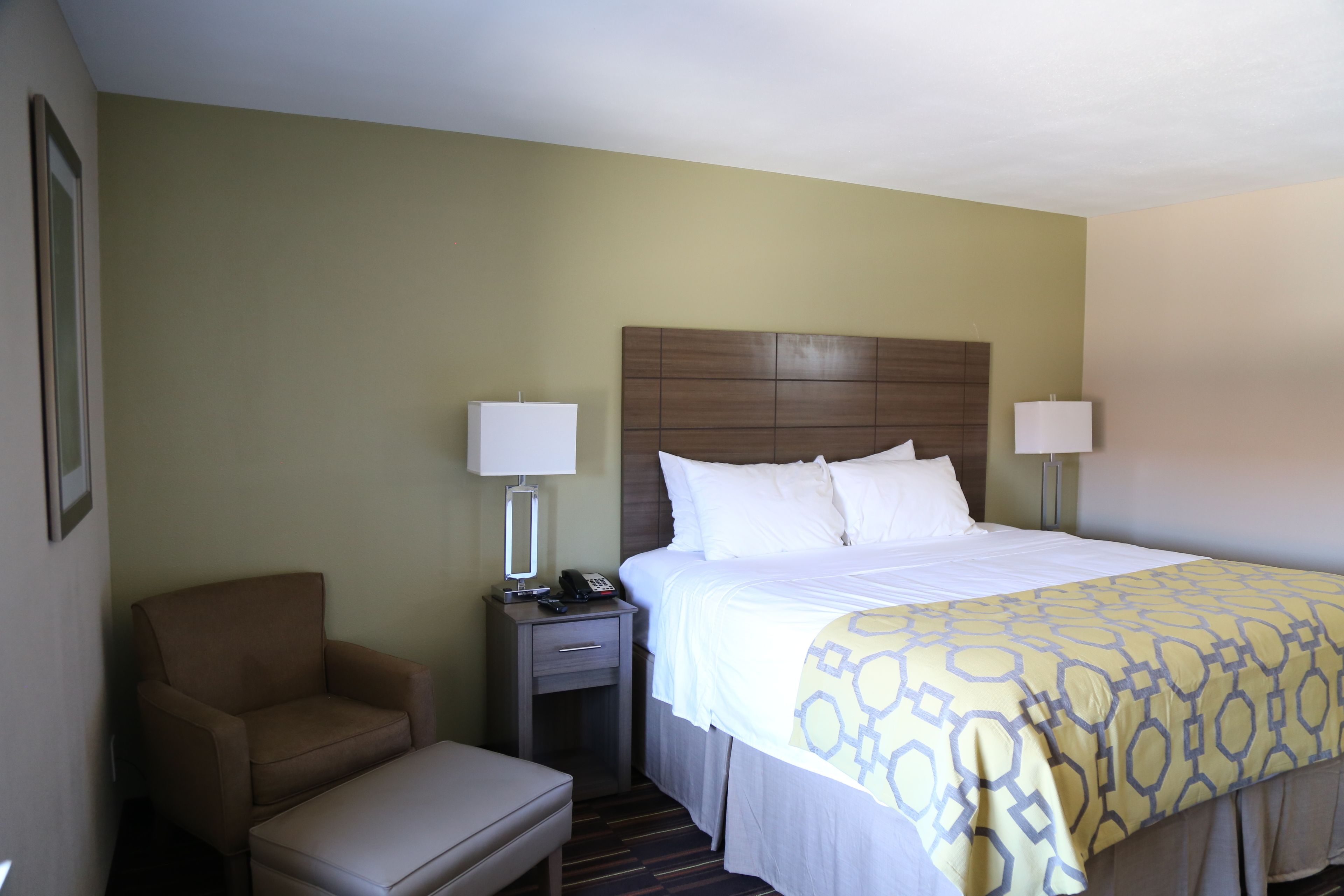 A hotel room with a bed, bedside lamps, a chair, a nightstand, and a desk.