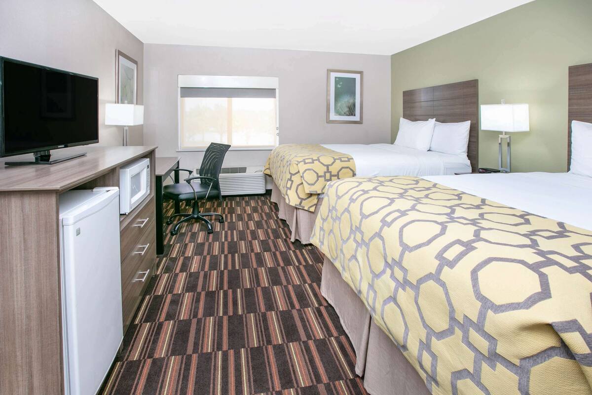 A hotel room with a TV, desk, chair, two beds, and a window.