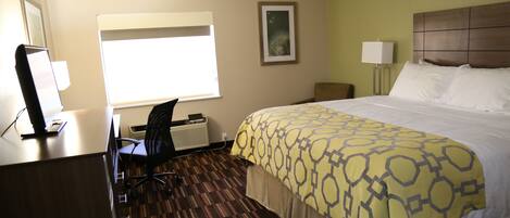 Una habitación de hotel con una cama grande, un escritorio con una computadora, una silla, una ventana y una lámpara de pared.