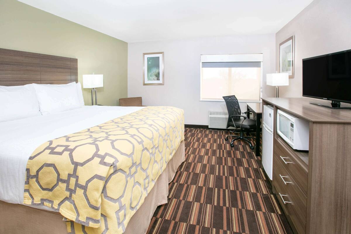A hotel room with a large bed, a desk with a chair, a television, and a dresser.