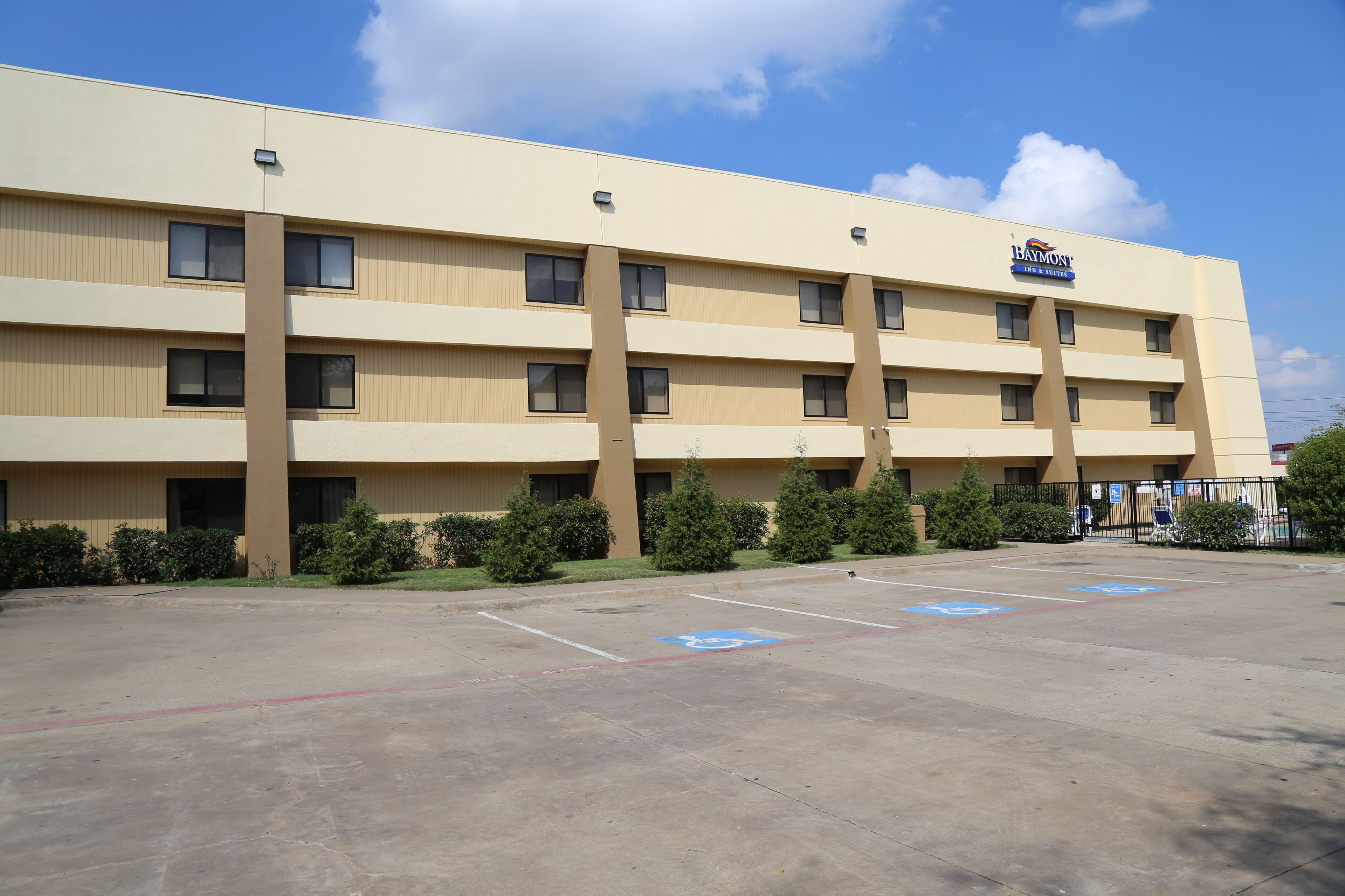 A multi-story hotel with a flat facade, parking lot with handicapped accessibility, and a clear blue sky.
