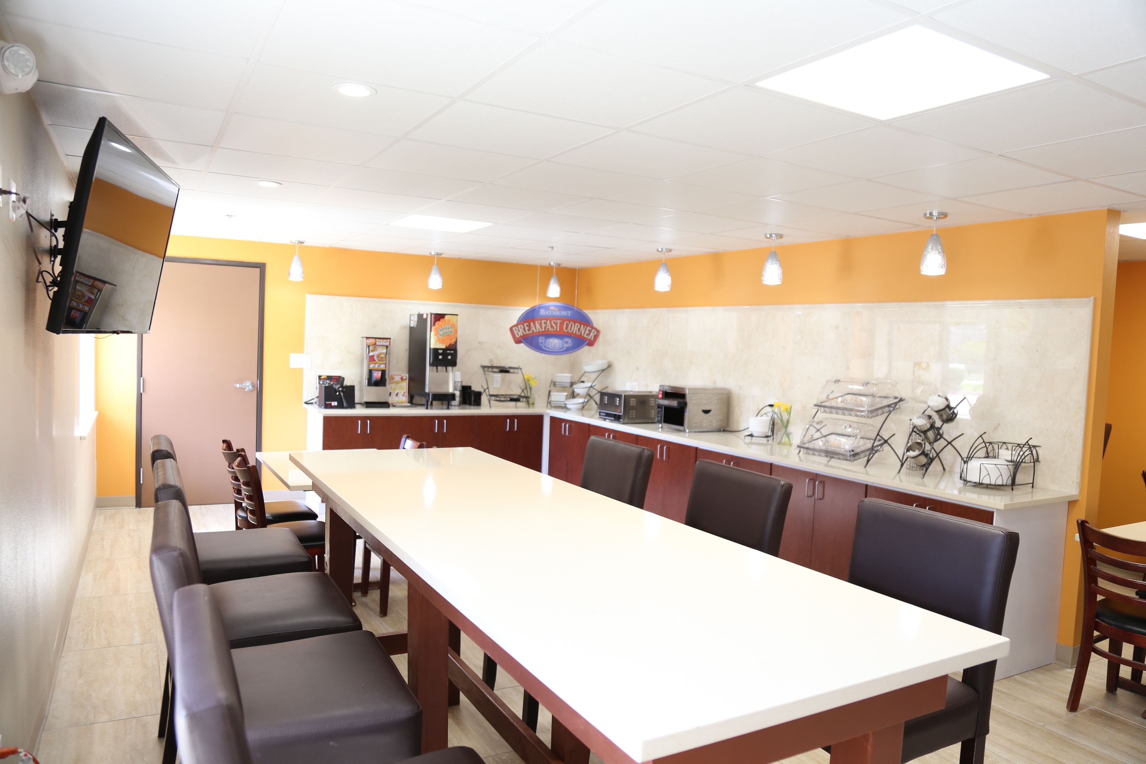 A breakfast corner with a long table, chairs, and kitchen appliances.