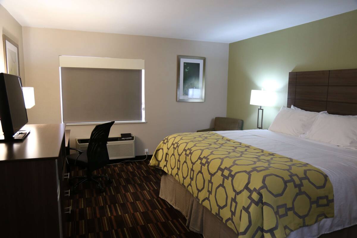 A hotel room with a bed, desk, chair, and a window.