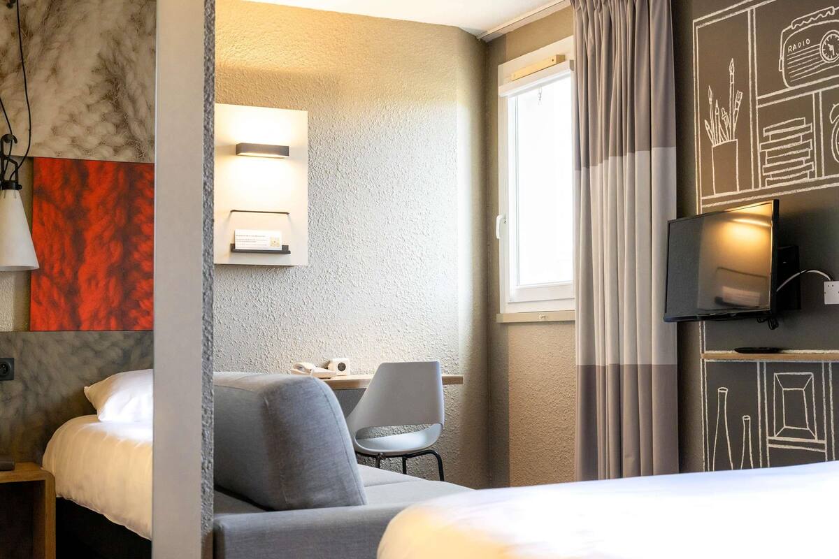 A hotel room with a bed, a desk, a chair, a TV, and a window with curtains.