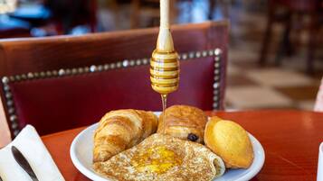 Een bord eten met croissants en een pannenkoek waar stroop op wordt gegoten.