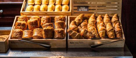 A bakery display with various baked goods, including bread and pastries, in wooden crates labeled "ibis kitchen".