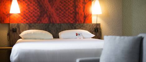 Ein Hotelzimmer mit einem Bett, zwei Nachttischlampen, einer Kopfteil und einem Wandbild.