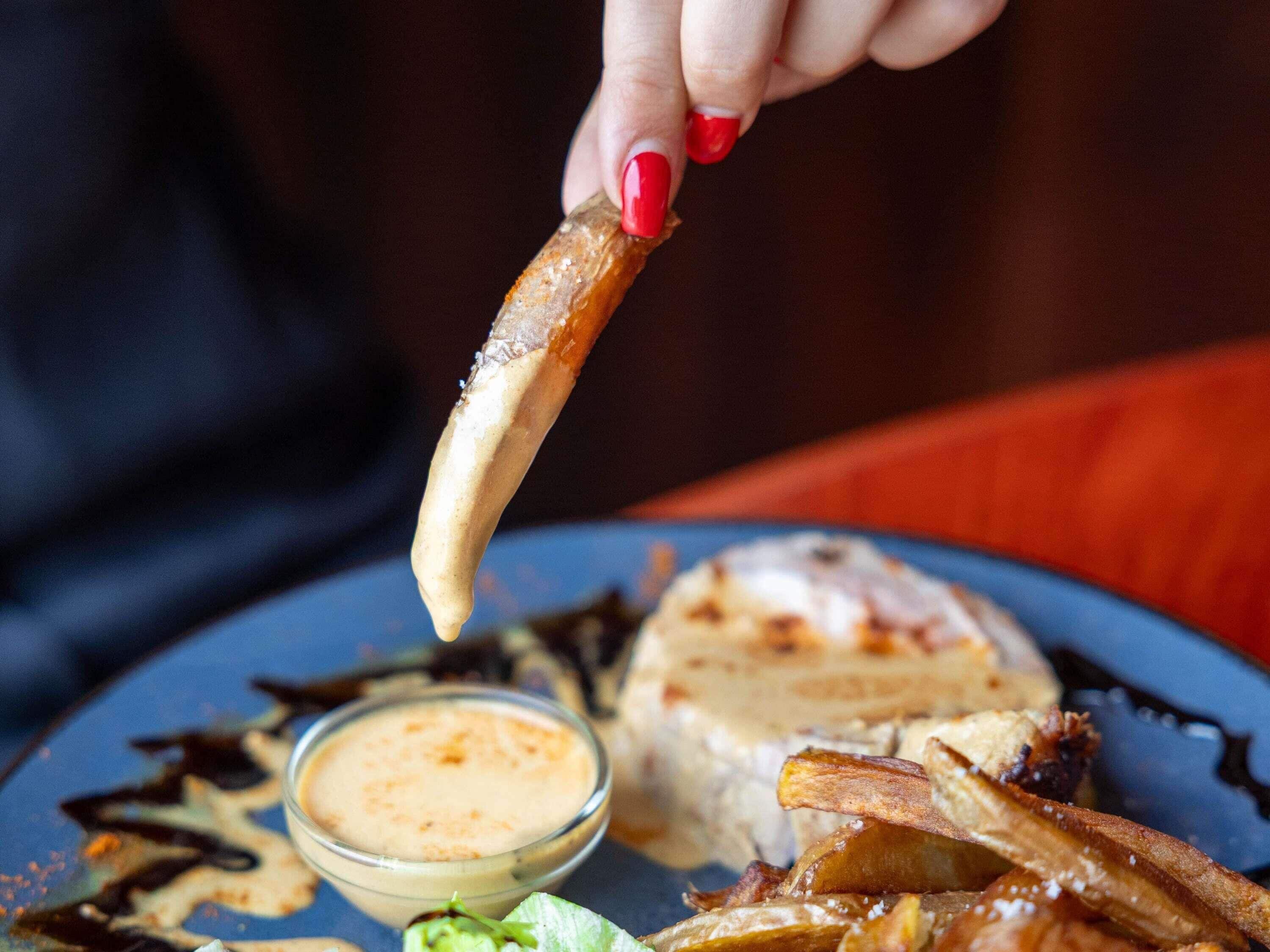 Une assiette contenant divers aliments, notamment un morceau de viande, un bol de sauce et un morceau de pain.