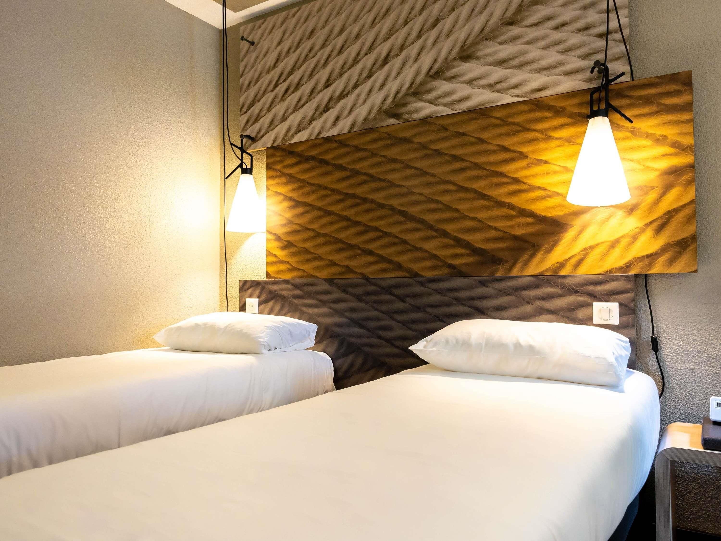 A hotel room with two beds, a textured wall, and pendant lights.